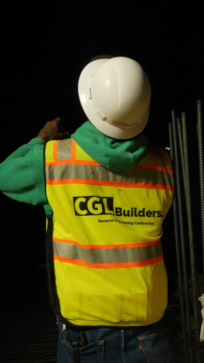 Worker in a CGL Builders vest on a night job site