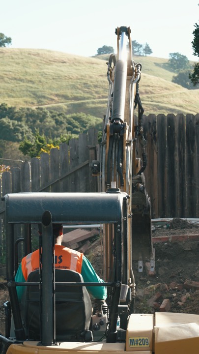 Excavator arm working by a wooden fence with golden hills behind